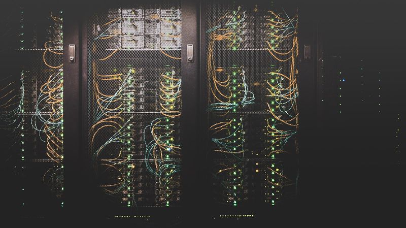 Server racks in a data center with glowing green indicator lights and tangled network cables