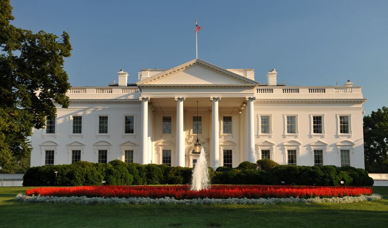 The north facade of the White House in Washington, D.C., with a fountain and flower beds in the foreground under a clear blue sky